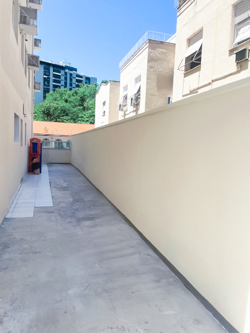 Corredor estreito do condomínio L’Essence Laranjeiras com piso recém-aplicado e paredes repintadas em tom claro, iluminação natural e vista limpa após a reforma.