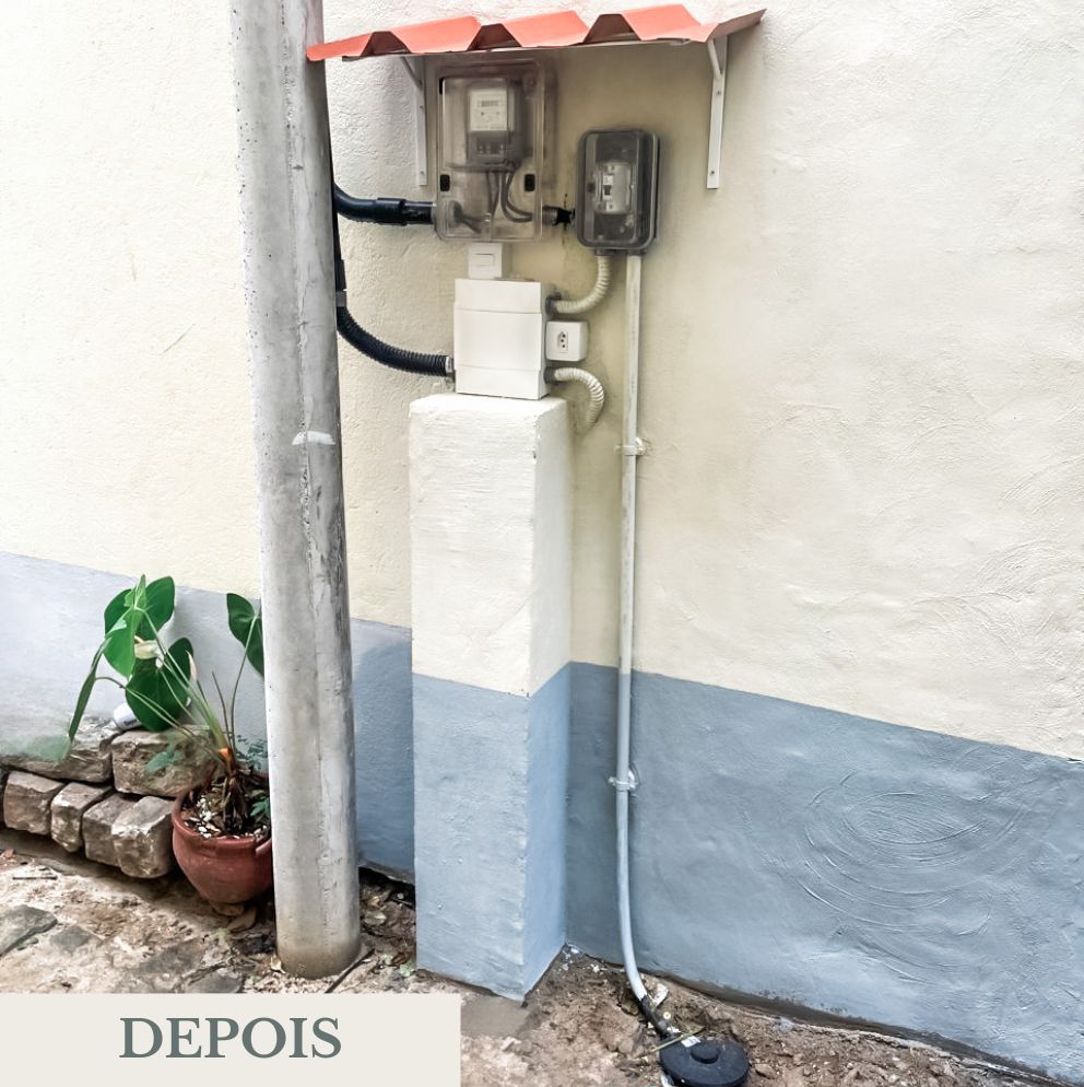 Painel de energia reformado externo com novo abrigo de chapa vermelha, fiações organizadas e parede repintada em tom claro com faixa inferior azul.