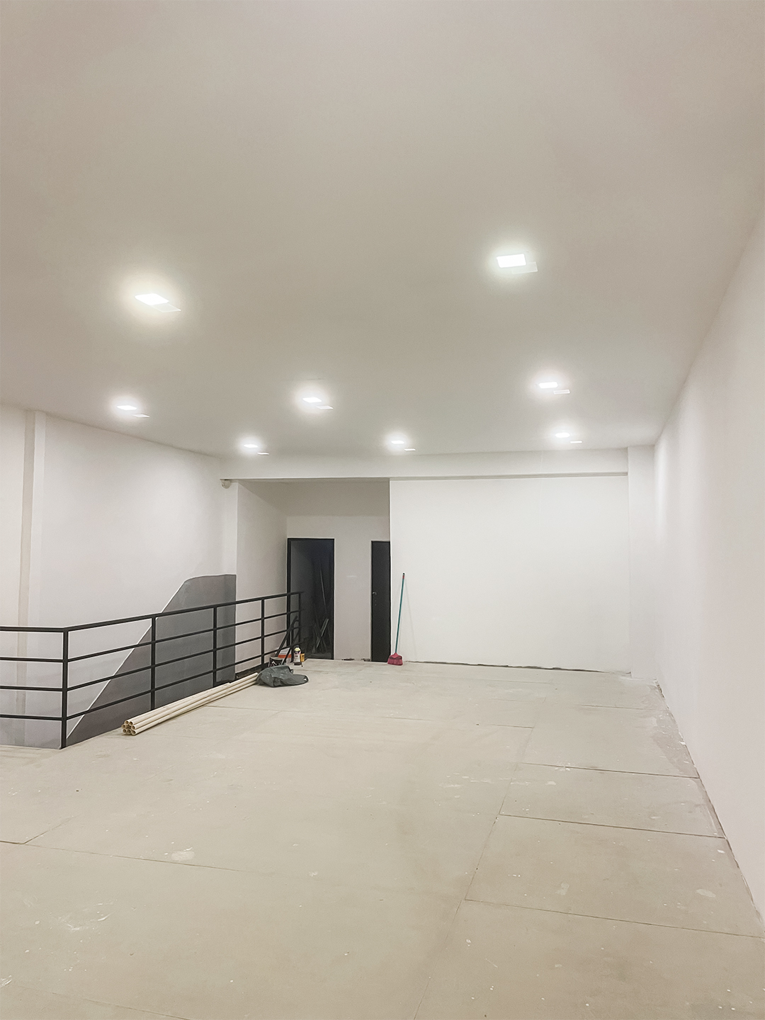 Mezanino finalizado com salão amplo, piso claro, paredes brancas, iluminação embutida no teto e guarda-corpo metálico preto.