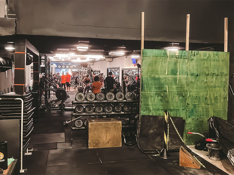 Sala de treinamento da academia antes da reforma, com halteres, equipamentos de musculação, espelhos e área isolada para o início das obras.