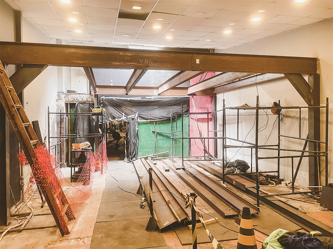 Área interna da academia em reforma com estrutura metálica instalada, materiais de obra no piso, escada lateral e espaço em fase de transformação.
